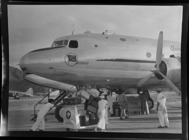 Baggage is loaded into a Qantas Empire Airways Douglas DC-4 (VH-EBK) Skymaster aircraft at Kai-Tak Airport, Kowloon, Hong Kong