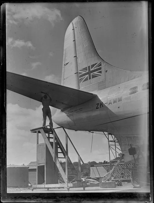 Unidentified man working on the tail wing of the Tasman Empire Airways Ltd Solent aircraft, Mechanics Bay, Auckland