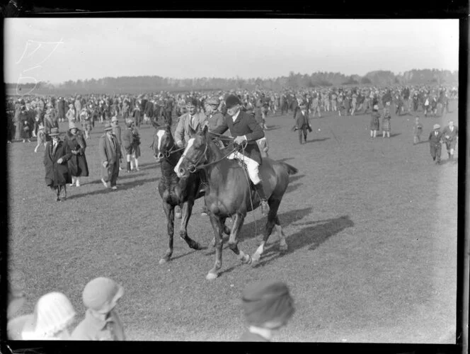 Two unidentified men on horseback amongst the crowds at the Pakuranga point to point hunt, Auckland