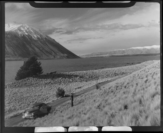 Unidentified man [Harry Wigley?] and Chevrolet sedan car on the road alongside Lake Ohau, Waitaki County