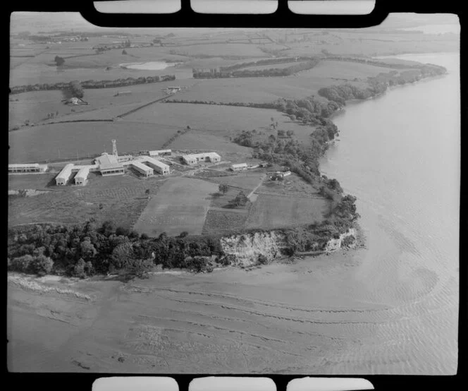 Pakuranga, East Auckland, view of health camp with buildings and tower, surrounded by farmland, overlooking estuary foreground