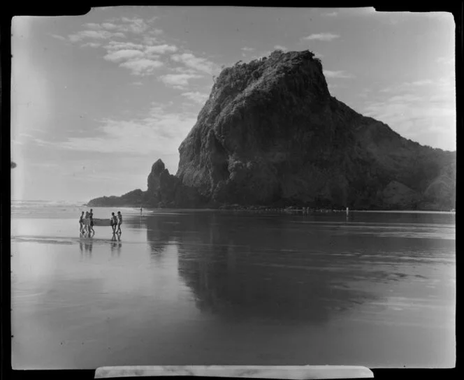 Beach at Piha, Auckland, showing Lion Rock and people carrying a dinghy
