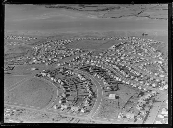 View of new housing development Glen Innes, Auckland City, showing Pilkington Road, Hobson Drive to Dunkirk Road with school by tidal estuary, looking to Half Moon Bay with farmland beyond