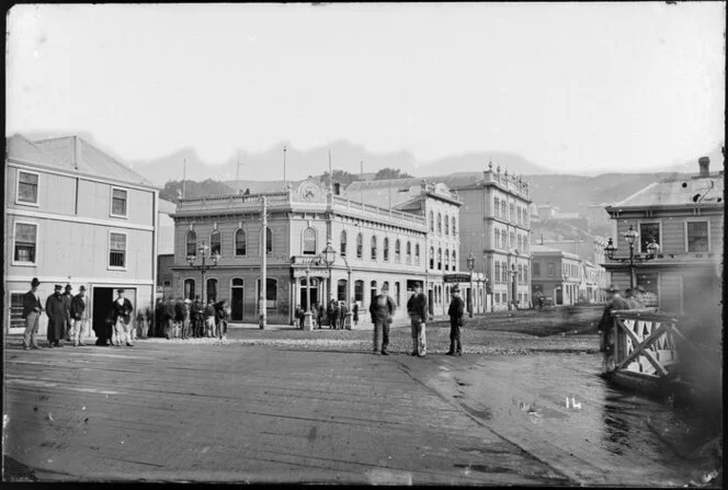 Intersection of Grey Street and Customhouse Quay, Wellington, showing groups of men standing in street, and buildings the Pier Hotel, Post Office Hotel, and the post office
