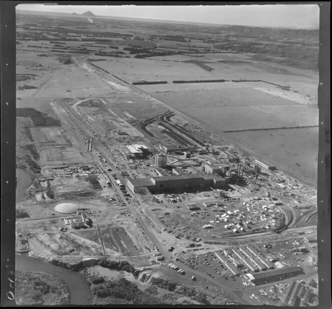 Kawerau, Bay of Plenty, showing Tasman Pulp and Paper Mill under construction to Tamarangi Drive (State Highway 34) with farmland beyond