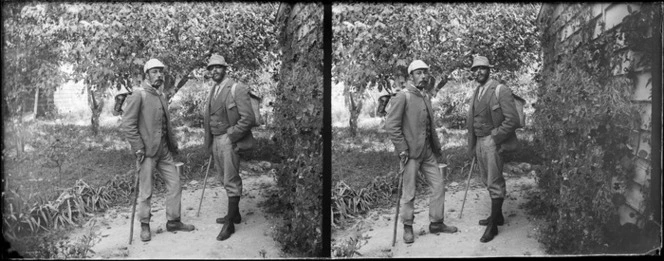 Photographer William Williams and an unidentified man, who is wearing sunglasses and smoking a pipe, in a garden and dressed for a journey on foot [hike? tramp?], [ Williams' Carlyle Street house, Napier, Hawkes Bay Region?]