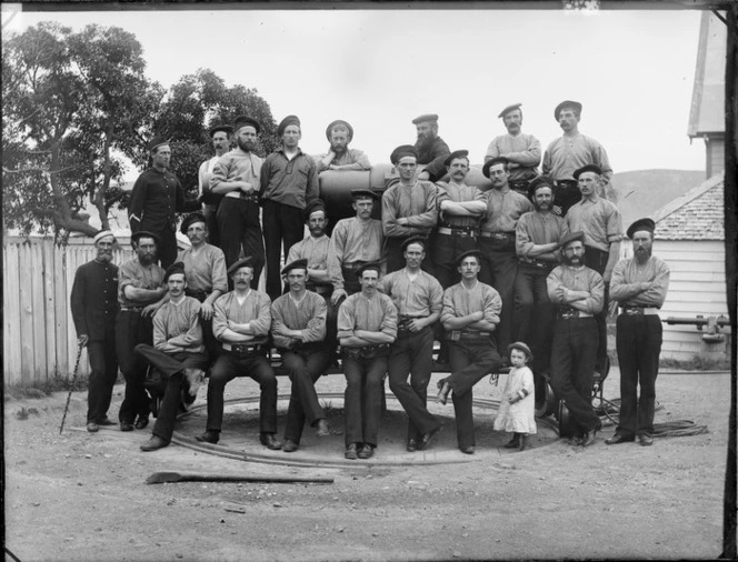 Men in uniform and one small child pose with cannon at the Mt Cook Barracks, Te Aro, Wellington