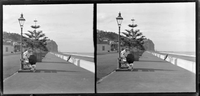 Marine Parade, Napier, including a woman seated on a park bench holding an umbrella