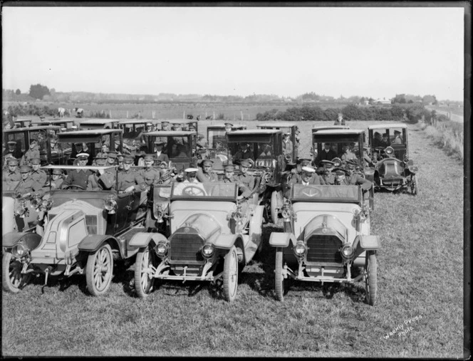 World War I invalided troops arrive home, transported in cars lined up in three rows on a field, front row cars open topped, farmland beyond