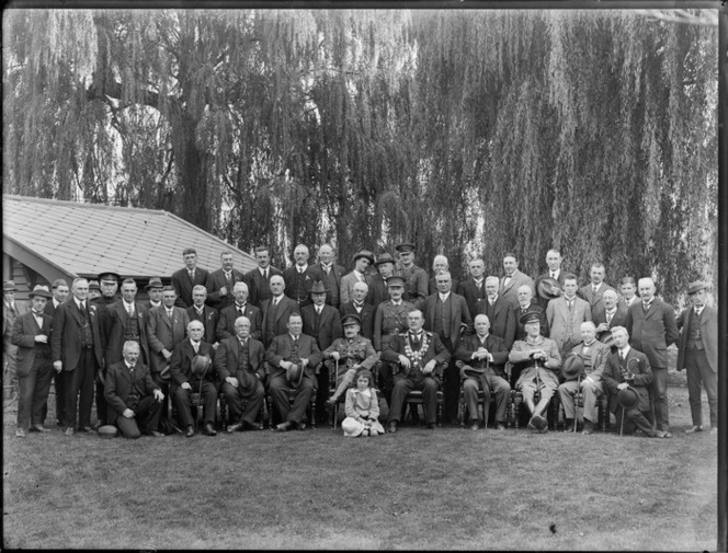 Mayoral reception, group of men in front of tree posing for group photograph with Sir F H D Bell and Dr Thacker, young girl kneeling in front, group includes several military men and Mayor with Chain of Office