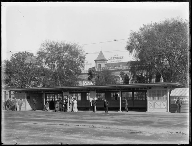 Cathedral Square, Christchurch, showing tram shelter, Central Post Office , and signs advertising The Dresden Piano Company and J Porter, builder and contractor