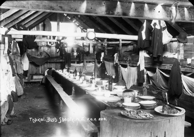 Interior of a hut in a timber camp, with a dining table set for a meal in the centre, and bunk beds set around the walls