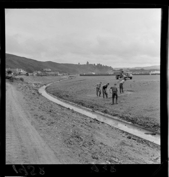 Canal drain from Naenae to Waddington Drive, Lower Hutt, including council workers sowing the lawns at Naenae Park in the foreground