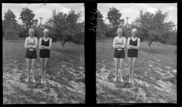 Image: Two unidentified girls wearing swimsuits and bathing caps, standing on grass, location unidentified