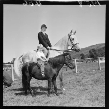 Image: Unidentified woman rider and unidentified child on a miniature horse, during the 1958 A&P (agricultural and pastoral) show at Trentham, Upper Hutt