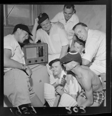 Image: Group of unidentified cricketers gathered around a radio listening to the races