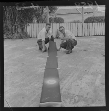 Image: Two unidentified men with a strip of film on the concrete outside for a cartoon being produced in Levin