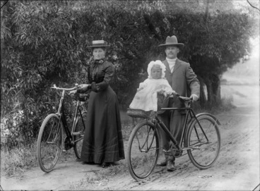 Image: Unidentified man and woman with bicycles, a little girl is sitting in a cane seat attached to the handlebars, probably Christchurch district