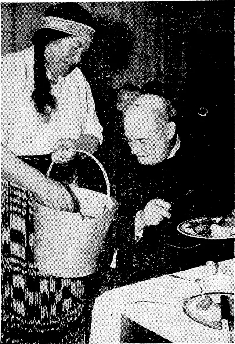 Image: v ■ '"Sydney Morning Herald" Photo. Pork and vegetables cooked in Maori fashion being served to Canon Hammond by Mrs. H. W. Wehi at Hammondville, N.S.W., last week when the Maori choir was in Sydney. Members of the Maori choir ■ prepared and cooked all the food in the open air. (Evening Post, 06 August 1938)