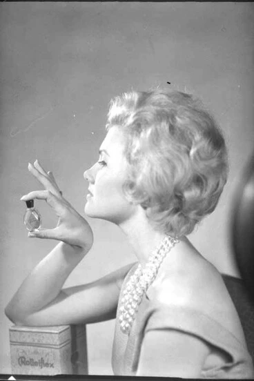Image: Head and shoulders portrait of Miss Valda Adams, holding a bottle of perfume