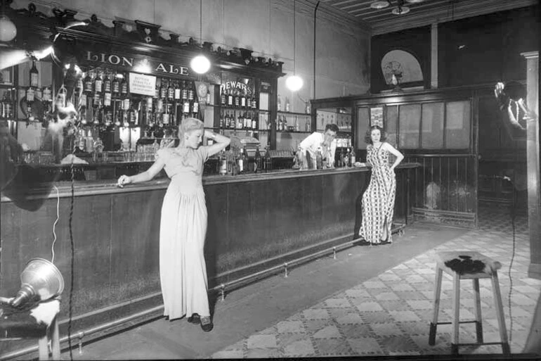 Image: Showing the interior of the Occidental Hotel, Vulcan Lane, Auckland, with two models and a barman