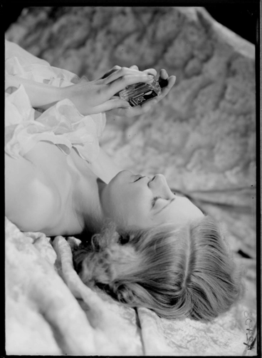Image: 1/4 length portrait of a model lying down holding a cosmetic bottle, for Sargood Son and Ewen 1940