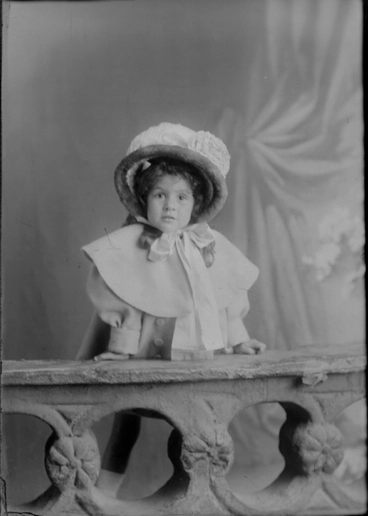 Image: 3/4 length portrait of Missie Kissling, leaning on a low wall,....