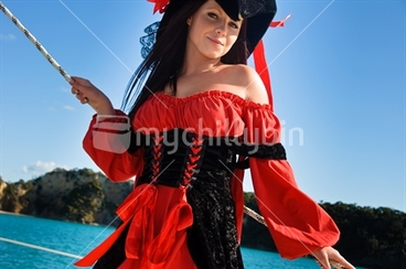 Image: Young smiling european women in bright red pirate costume on the railing of a sailing boat, Bay of Islands, New Zealand