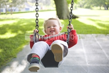 Image: A young blonde boy on a playground swing
