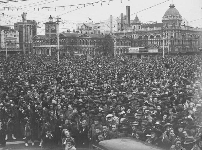 Image: Celebrations. Crowd at WWII, Victory over Europe ( VE ) Day Celebration. Held 9 May 1945, Pipe Bandsman front Left. Cathedral Square, Christchurch, Canterbury, New Zealand.
