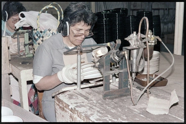 Image: Negative - Worker sitting at mounted machine, holding stack of plates applying colour or similar