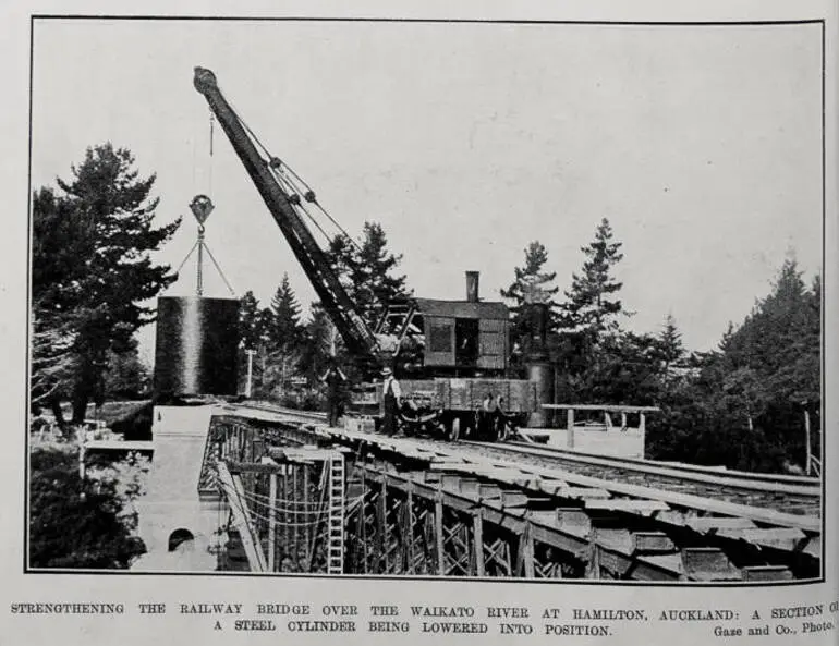 Image: STRENGTHENING THE RAILWAY BRIDGE OVER THE WAIKATO RIVER AT HAMILTON, AUCKLAND: A SECTION OF A STEEL CYLINDERS BEING LOWERED INTO POSITION