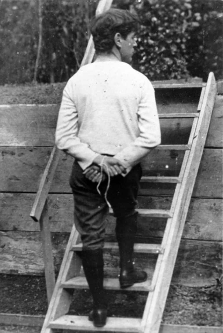 Image: A theatrical scene of a man with his hands tied behind his back