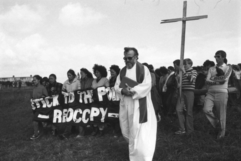 Image: Father Terry Dibble leading protestors with cross and banner 'Stick to the Point Reoccupy'. Auckland Orakei Bastion Point