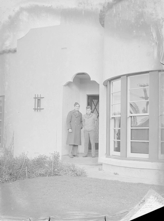 Image: [Two military servicemen pose in front of house]