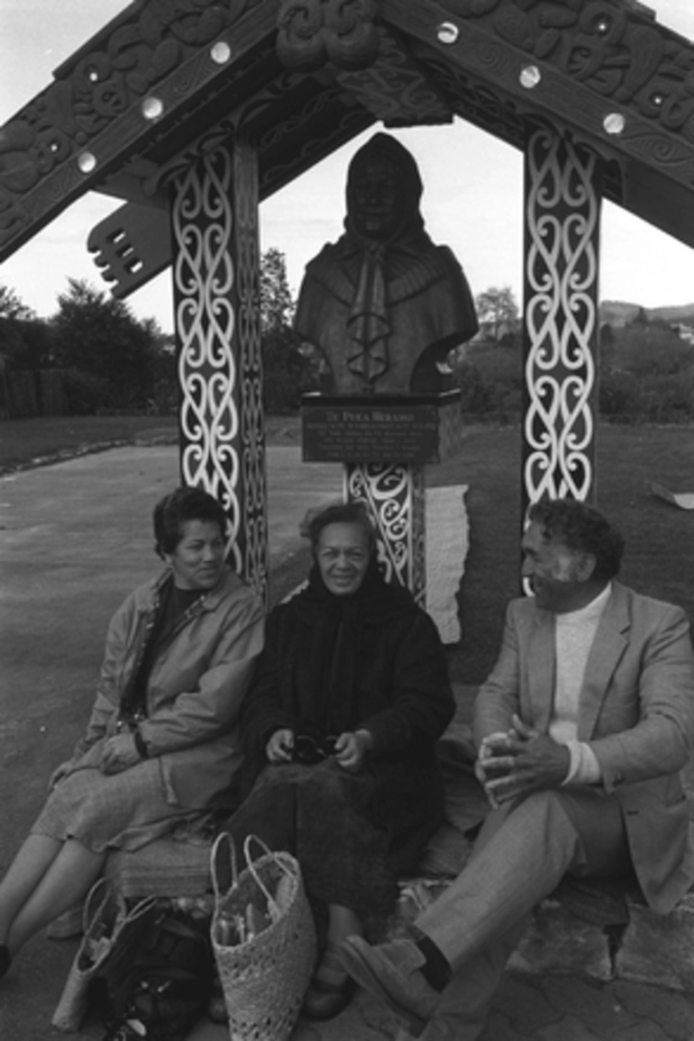 Image: Trio seated outside in front of bust of Te Puea Herangi. National Hui, Turangawaewae Marae, Ngaruawahia