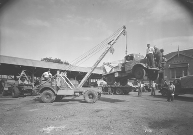 Image: [Truck with hoist lifting a tow-truck]