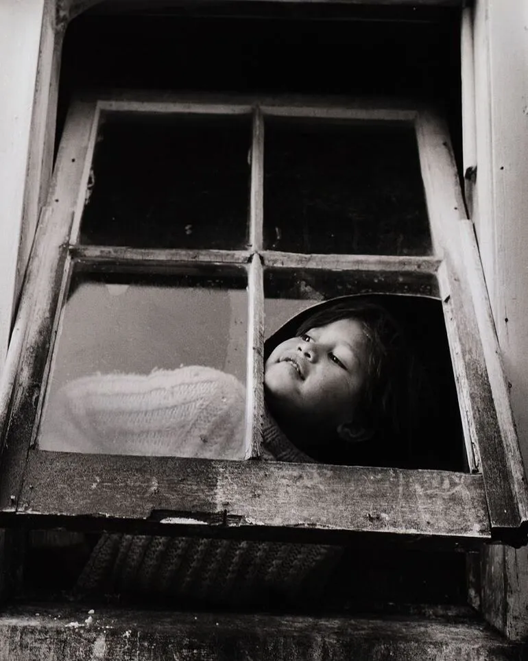Image: Mutu has to climb up on a box to look through the big old window at the back of the house. From the series: Washday at the pa