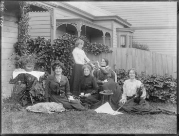 Image: Unidentified women having a tea party outdoors, probably Christchurch district, one woman holds a violin, while a girl serves food from a plate