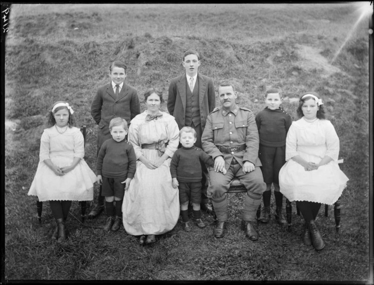 Image: Family portrait on grass hillside, unidentified parents with their two older sons and two daughters, and three young sons, father in soldier's uniform, probably Christchurch region