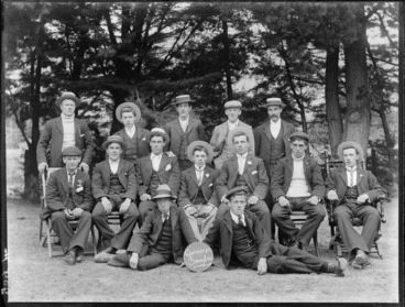 Image: Group portrait of unidentified men in straw hats and caps, with 'Summer Camper' sign in front, pine trees beyond, Sumner, Christchurch