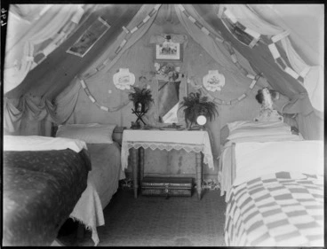 Image: Interior of a tent, showing four beds and a dressing table, with paper decorations strung around walls, and printed reproductions of paintings attached to roof, possibly Christchurch district