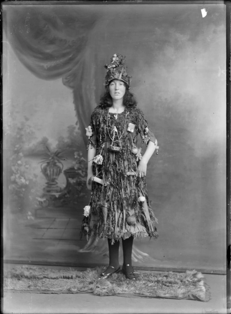 Image: Studio portrait of unidentified young woman in Christmas tree fancy dress and hat costume, with little presents and decorations hanging off her, Christchurch