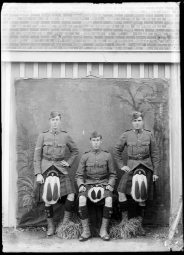 Image: Group of three unidentified soldiers in kilts outside a building, with a painted studio backdrop, probably Christchurch district