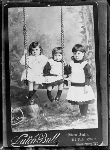 Image: Three unidentified little girls, two on a swing and one holding onto rope, - Photograph taken by Dutch & Bull, Christchurch