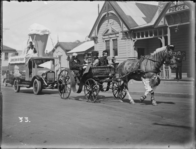 Image: New Napier Week Carnival, men in costumes with horse and buggy, Police Station behind with Police Officer looking on, Napier, Hawke's Bay District