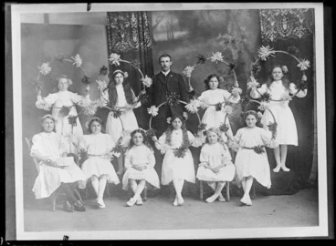 Image: Studio portrait of unidentified ten young girls wearing hair ribbons and holding hula hoops decorated with small pompoms, standing with a man with a moustache, Christchurch