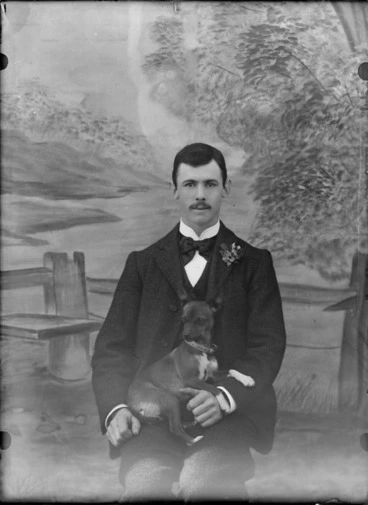Image: Studio portrait of unidentified young man with moustache, bow tie, carnation and puppy on his knees, Christchurch