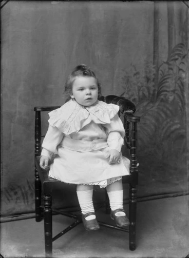 Image: Studio portrait of unidentified young girl with large laced collar or shoulder cape, sitting in wooden chair, Christchurch