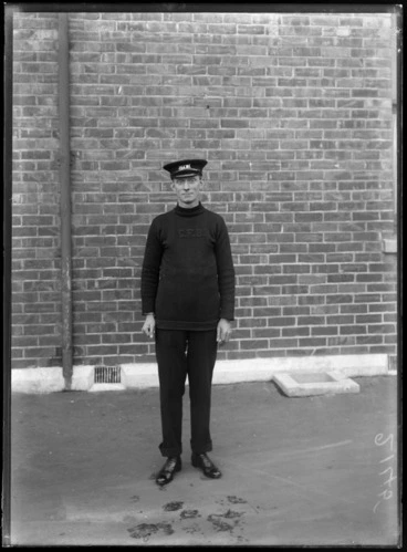 Image: An unidentified member of the Christchurch Fire Brigade, wearing a woolen jersey with the letters 'CFB' embroidered on front, and a peaked cap with insignia, possibly Christchurch district